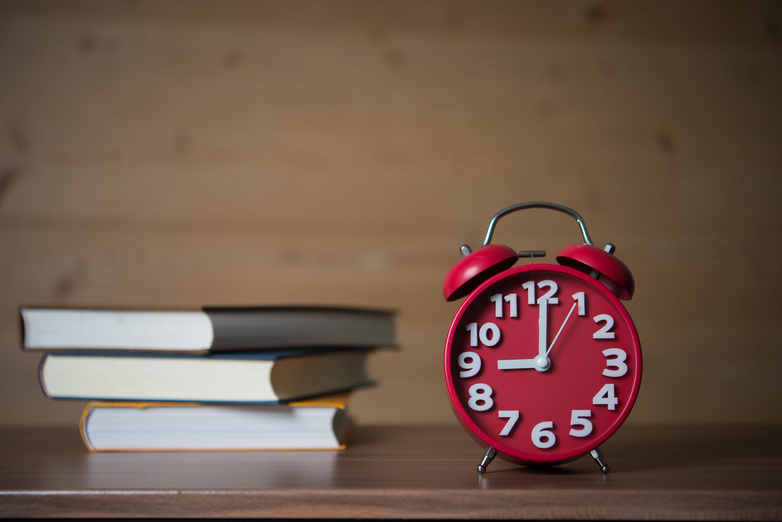 Alarm clock at 9am and stack of books with cup of coffee on wood
